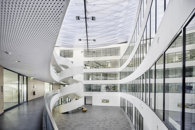 Modernes Atrium mit geschwungenen weißen Wänden, spiralförmiger Treppe und transparentem Folienkissendach im Lilienthalquartier.